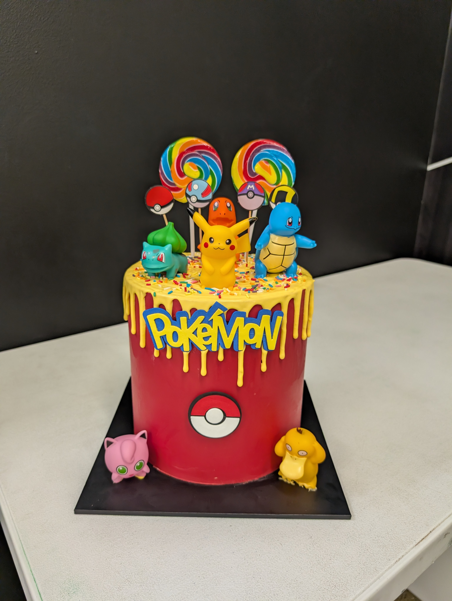 Red and yellow drip Pokemon birthday cake with Pikachu Charmander Squirtle Bulbasaur and rainbow lollipops