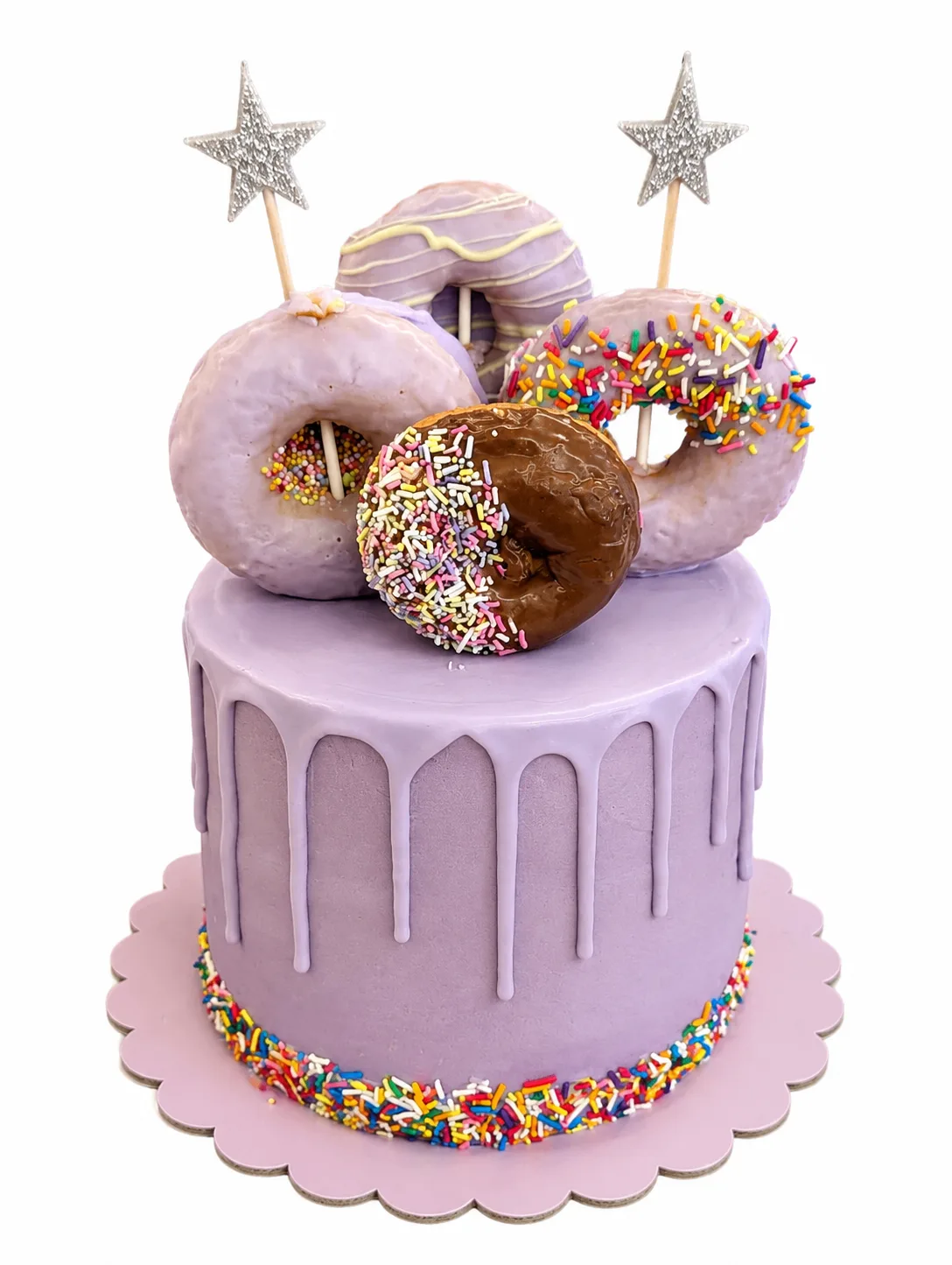 Lavender drip cake topped with assorted donuts and rainbow sprinkles
